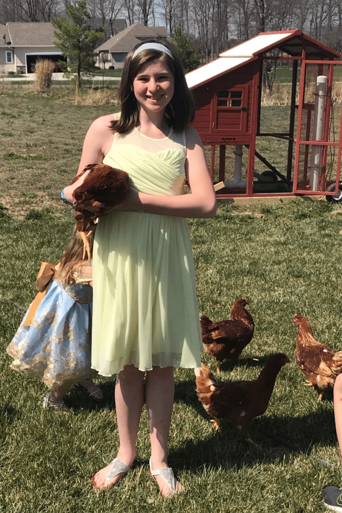 Daughter-in-yellow-dress-holding-bovans-brown-chicken-in-front-of-red-coop