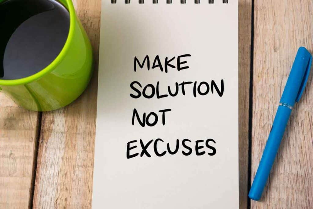 coffee and notepad on table with "make solutions not excuses" written in black marker 