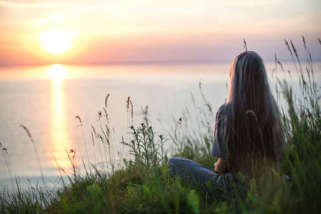 woman sitting by the bank of a lake looking across to the other side